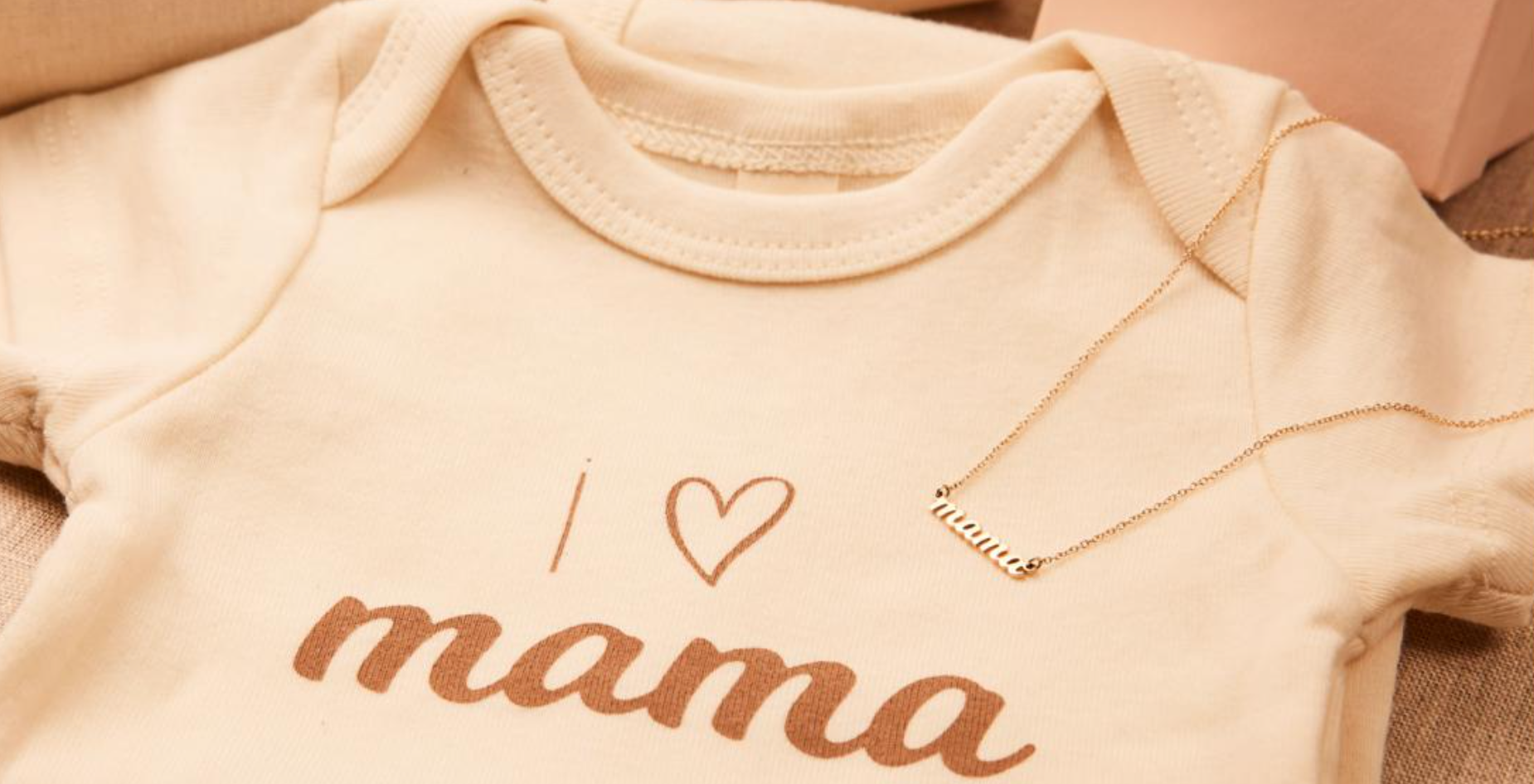 A baby onesie and delicate gold chain with the words 'I Love Mama' on both.