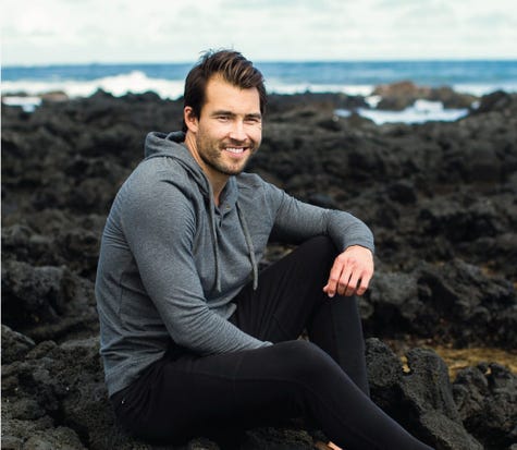 A man wearing a comfortable Cariloha hoodie while sitting on dark volcanic rocks.