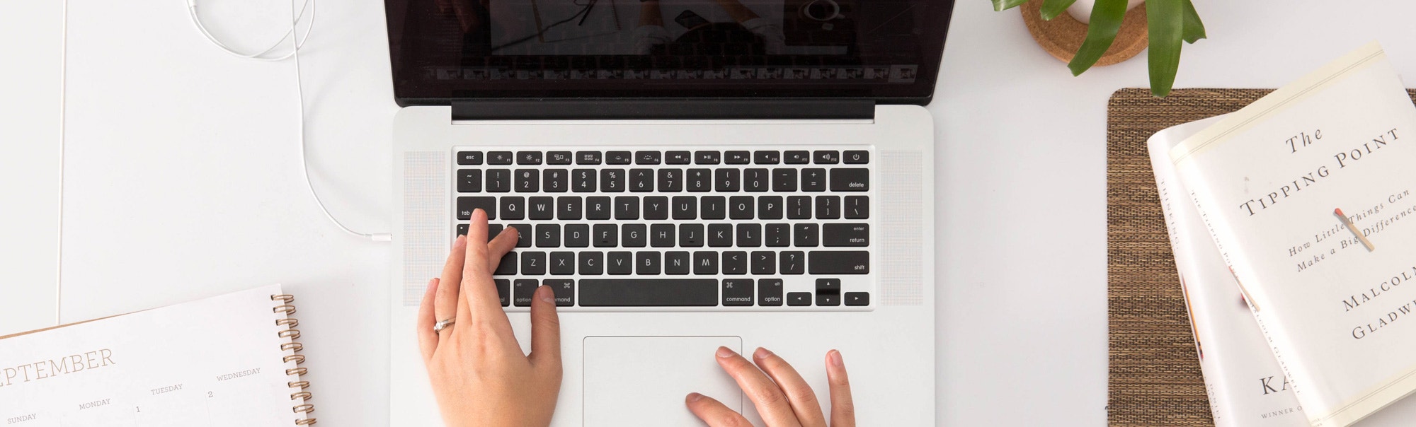 An open laptop on a desk with someone busy typing on it. 