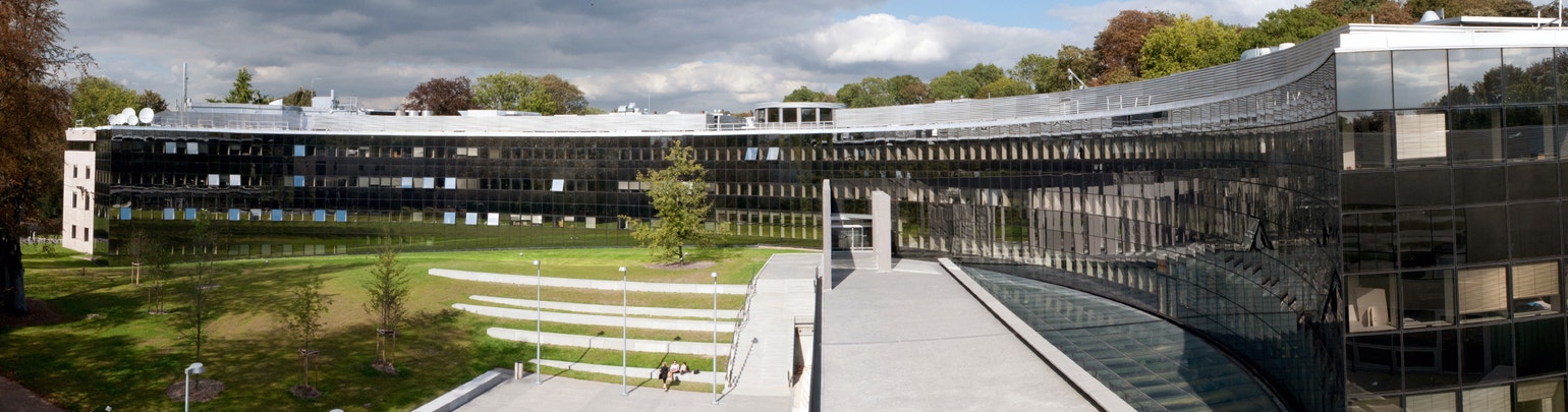 A large modern glass and steel building surrounded by lush green trees.