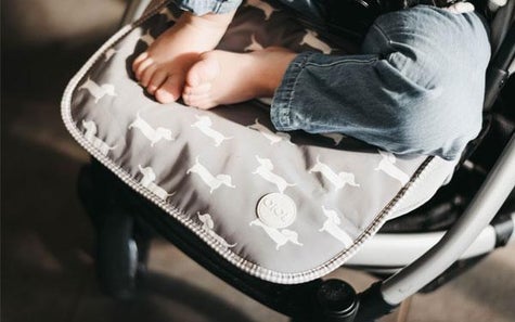 A baby wearing jeans on a grey pram liner with a wiener dog pattern on it. 