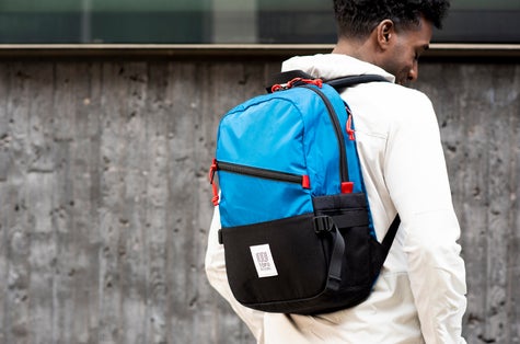 A man in a white Topo Designs shirt with a vibrant blue Topo backpack on.  