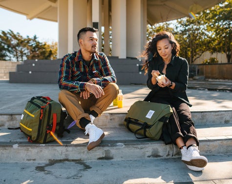 A man and woman enjoying an ice cream together. Topo Designs bags are at their feet. 